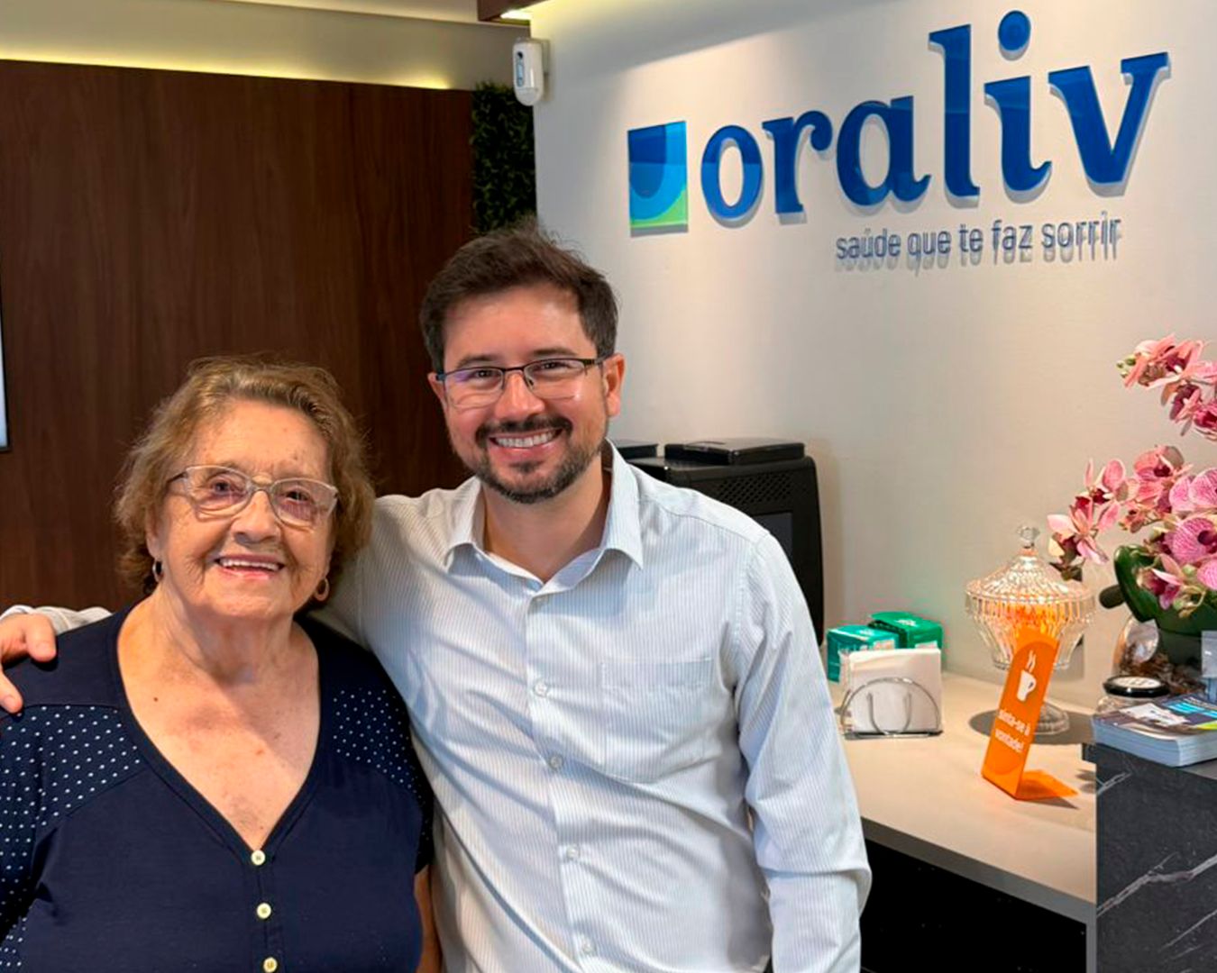 Paciente sorrindo com o Dr. Paulo Fernando na recepção da clínica Oraliv